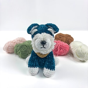 May include: A teal blue crocheted miniature schnauzer dog toy with white fur accents and a brown crocheted collar. The dog toy is surrounded by balls of yarn in various colours.