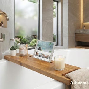 Könnte beinhalten: Ein rechteckiges Badewannenablage aus Holz, das über einer weißen Badewanne liegt. Auf der Ablage befinden sich eine kleine Sukkulente im Topf, ein Glas mit Holzlöffel, ein Tablet mit einer Spa-Website, eine Kerze im Glas und ein beiges Handtuch.