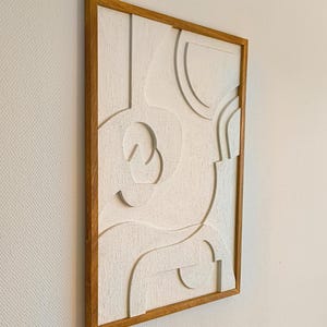 Seitliche Ansicht eines abstrakten 3D Wandreliefs im Format 76 x 56 x 2 cm, gefertigt aus CNC-gefrästem MDF mit strukturierter Oberfläche in natürlichem Cremeweiß. Der hochwertige Rahmen aus massivem, handgeöltem Eichenholz betont das minimalistische Design. Ideal als moderne Wanddekoration für Wohnzimmer, Flur, Büro oder Schlafzimmer im Japandi-, Skandi- oder zeitlosen Stil. Handgefertigte Wandkunst aus natürlichen Materialien.