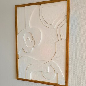 Seitlich aufgenommene Gesamtansicht eines handgefertigten 3D Wandreliefs im Format 76 x 56 x 2 cm, bestehend aus CNC-gefrästem MDF mit strukturierter Oberfläche in Cremeweiß und massivem, geöltem Eichenholzrahmen. Die Perspektive zeigt die Tiefe und harmonische Linienführung des abstrakten Designs. Ideal als hochwertige Wanddeko im Wohnzimmer, Büro, Flur oder Schlafzimmer – minimalistischer Japandi-Stil mit natürlichen Materialien.