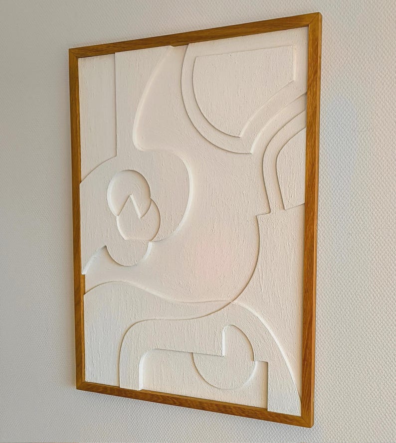 Seitlich aufgenommene Gesamtansicht eines handgefertigten 3D Wandreliefs im Format 76 x 56 x 2 cm, bestehend aus CNC-gefrästem MDF mit strukturierter Oberfläche in Cremeweiß und massivem, geöltem Eichenholzrahmen. Die Perspektive zeigt die Tiefe und harmonische Linienführung des abstrakten Designs. Ideal als hochwertige Wanddeko im Wohnzimmer, Büro, Flur oder Schlafzimmer – minimalistischer Japandi-Stil mit natürlichen Materialien.