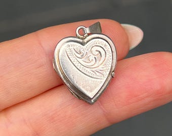 May include: Silver heart-shaped locket with an intricate engraved design. The locket has a hinged opening and is perfect for holding a small photo or memento.