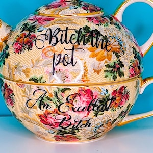 Puede incluir: Juego de té decorativo con tetera y taza, con un estampado floral en amarillo, rosa y verde. La tetera tiene el texto "Bitch the pot" y la taza "An Excellent Bitch".