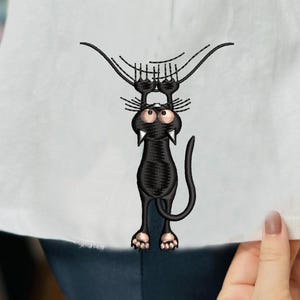 May include: White t-shirt featuring a black embroidered cat design. The cat is hanging upside down, with large eyes and fangs. The design is detailed with whiskers and paw pads, creating a whimsical and playful aesthetic.