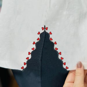 May include: White shirt with a black and red heart trim detail. The trim is a scalloped design with red hearts along the edge.