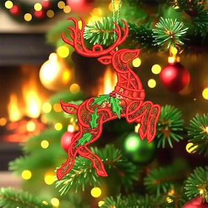 以下が含まれることがあります： 複雑な透かし彫りのディテールが施された、赤いトナカイの形をしたクリスマスオーナメント。トナカイには緑色のヒイラギのアクセントがあり、緑色の紐から吊り下げられています。オーナメントは、赤と緑のオーナメントが付いたクリスマスツリーに飾られています。