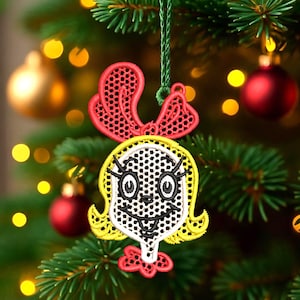 May include: Embroidered Christmas tree ornament featuring a cartoon face with yellow hair, a red bow, and a white face with black details. The ornament is hanging on a Christmas tree with red and gold ornaments.