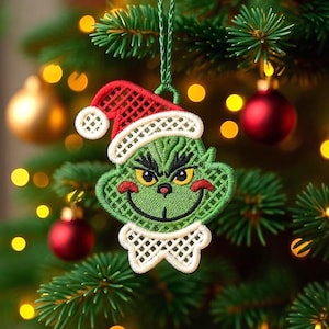 Puede incluir: Un adorno navideño verde con la forma de un personaje que lleva un gorro de Papá Noel rojo con ribete blanco y un cuello blanco. El adorno cuelga de un árbol de Navidad con adornos rojos y dorados y luces amarillas.