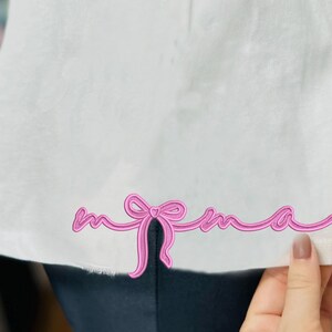 May include: White t-shirt with a pink ribbon design that spells out "mama" on the bottom hem.