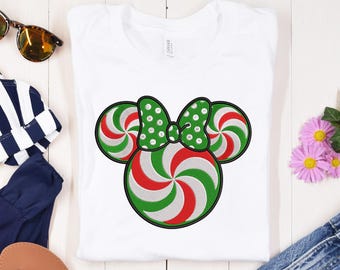 May include: White t-shirt with an embroidered design of a candy cane Minnie Mouse head. The candy canes are red and green with white swirls.