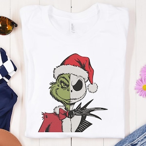May include: A white t-shirt featuring a green and grey illustration of the Grinch and Jack Skellington from Nightmare Before Christmas. The Grinch is wearing a Santa hat and a red bow tie. The illustration is in a cartoon style.