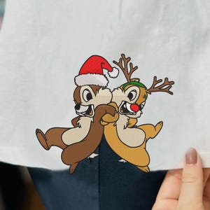 May include: Chip 'n Dale are dressed up for the holidays. Chip is wearing a Santa hat and Dale is wearing reindeer antlers. They are both smiling and hugging each other.