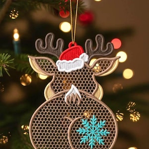 May include: Embroidered Christmas ornament shaped like a reindeer with a red Santa hat. The reindeer has brown antlers, a brown body with a honeycomb pattern, and a blue snowflake on its rear. The ornament hangs from a gold string.