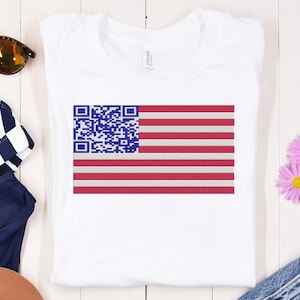 May include: White t-shirt with a blue and red American flag design. The flag has a QR code in the top left corner.