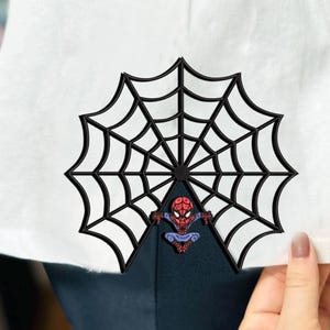May include: A black and white spider web design with a red and blue cartoon Spiderman character in the center.