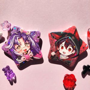 May include: Two star-shaped buttons with colorful anime characters. The button on the left features a purple-haired character with a pink and white outfit. The button on the right features a red-haired character with a black and red outfit.