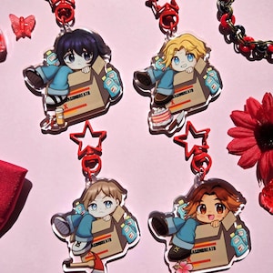 May include: Four colorful cartoon character keychains with red star charms. Each keychain features a character in a box with various items inside. The characters are a girl with black hair, a boy with blonde hair, a boy with brown hair, and a boy with brown hair. The boxes all have the text "Dragonbreath" on them.