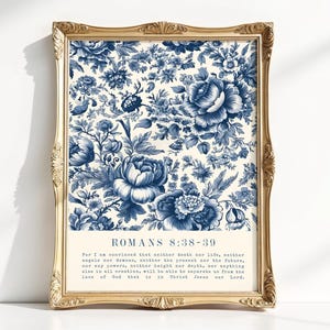 Op de afbeelding: Een rechthoekige wandkunstprint in een sierlijke gouden lijst met een blauw-wit bloemenpatroon. De print toont de tekst Romans 8:38-39 gevolgd door het volledige bijbelvers in een duidelijk, donkerblauw schreeflettertype op een crèmekleurige achtergrond.