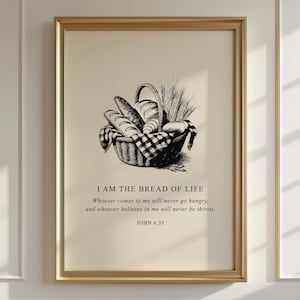 Op de afbeelding: Een ingelijste print met een zwart-wit illustratie van een mand vol brood en tarwe. De tekst "I AM THE BREAD OF LIFE" en een bijbelvers staan eronder. De lijst is goudkleurig.