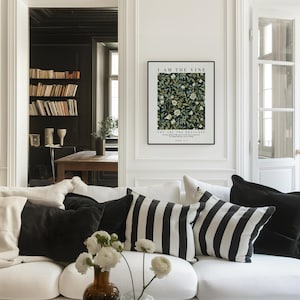 May include: A living room scene featuring a white sofa adorned with black and white striped and solid black pillows. A framed art print on the wall reads "I AM THE VINE" above a floral pattern. A vase of white flowers sits on the coffee table.