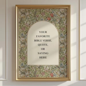 Op de afbeelding: Een rechthoekige wandkunstprint in een gouden lijst met een centrale crèmekleurige boog met de zwarte tekst: YOUR FAVORITE BIBLE VERSE, QUOTE, OR SAYING HERE. De rand toont een dicht botanisch patroon van bloemen en bladeren.