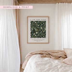 May include: A framed print with the text "I AM THE VINE" and "YOU ARE THE BRANCHES" over a dark green floral pattern. The print is in a light brown frame, and the background includes a bed with white linens and beige bedding.