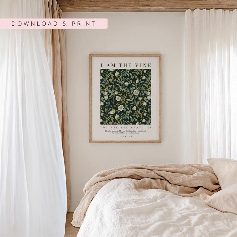 May include: A framed print with the text "I AM THE VINE" and "YOU ARE THE BRANCHES" over a dark green floral pattern. The print is in a light brown frame, and the background includes a bed with white linens and beige bedding.