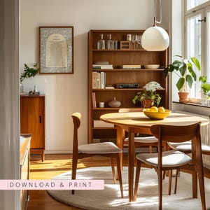 K&ouml;nnte beinhalten: Ein Esszimmer mit einem runden Holztisch und hell gepolsterten St&uuml;hlen, einem hohen Holzregal voller B&uuml;cher und Dekoration, einer wei&szlig;en Pendelleuchte und einem gerahmten Druck an der Wand mit dem Text "LITANY OF MORALITY".