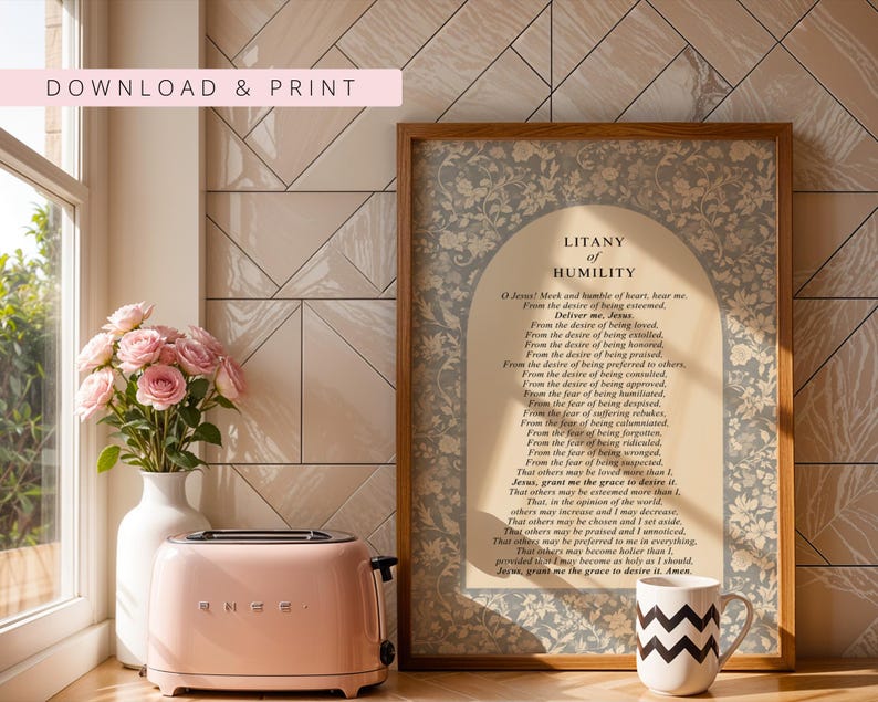 K&ouml;nnte beinhalten: Ein gerahmter Druck mit dem Text der Litanei der Demut, zentriert in einem beigen Bogenfeld, umgeben von einem blau-wei&szlig;en Blumenmuster. Der Druck befindet sich in einem Holzrahmen neben einem rosa Toaster und einer wei&szlig;en Tasse mit Zickzackmuster.