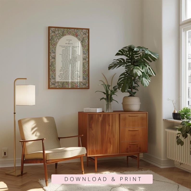 May include: A framed wall art print featuring the Litany of Humility text centred within an arched border, surrounded by a dense floral and botanical pattern in muted earth tones, displayed in a wooden frame on a light-coloured wall.