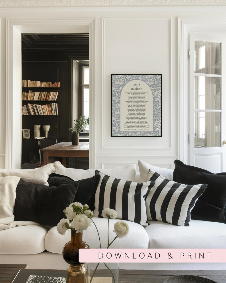 K&ouml;nnte beinhalten: Ein gerahmter Wandkunstdruck mit dem Titel Litany of Humility, der ein beiges, bogenf&ouml;rmiges Zentrum mit schwarzem Text zeigt, umgeben von einem blau-wei&szlig;en Blumenmuster. Der Druck h&auml;ngt an einer wei&szlig;en Wand &uuml;ber einem wei&szlig;en Sofa mit Kissen.