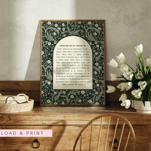 May include: A framed print of the Prayer of St. Francis, featuring a dark green floral pattern border. The text is centered on a cream-colored background. A basket and a vase of white tulips sit on a wooden dresser.