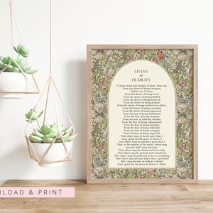 May include: A framed print featuring the Litany of Humility text centred within an arch, surrounded by a detailed floral pattern in shades of green, red, and tan. The print is displayed next to two white succulent planters in geometric frames.