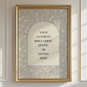 May include: A framed print with a gold-coloured frame. The artwork has a light grey floral pattern background and a cream-coloured arch shape in the centre with the text: "YOUR FAVORITE BIBLE VERSE, QUOTE, OR SAYING HERE."