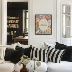 May include: A rectangular wall art print in a black frame featuring a floral border surrounding an oval center with the text "PRAISE GOD FROM WHOM ALL BLESSINGS FLOW" in black lettering, displayed on a white wall above a white sofa with pillows.
