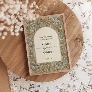 May include: A rectangular framed print featuring a cream-colored archway centered on a green floral background. The text reads: From His fullness we all received Grace upon Grace JOHN 1:16. The frame is light-toned wood with a thin profile.