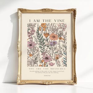 May include: A framed wall art print featuring a cream background with a colourful botanical illustration of wildflowers in shades of pink, orange, and green. The text reads I AM THE VINE, YOU ARE THE BRANCHES, and includes the verse John 15:5.