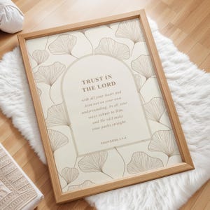 Puede incluir: Un estampado enmarcado con el texto "TRUST IN THE LORD" en fuente marrón claro. El estampado tiene un fondo beige con un patrón repetido de formas de hojas marrones claras. El marco es de madera marrón claro.