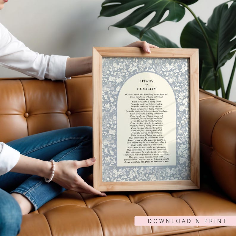 K&ouml;nnte beinhalten: Ein gerahmter Druck mit dem Text der Litanei der Demut, zentriert in einem cremefarbenen Bogenfeld, umgeben von einem hellblauen und wei&szlig;en Blumenmuster. Das Kunstwerk befindet sich in einem hellen Holzrahmen mit einem schlichten Rand.