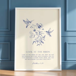 Op de afbeelding: Een ingelijste print met een crèmekleurige achtergrond en een blauwe bloemen- en kolibrie-illustratie. De tekst "LOOK AT THE BIRDS" staat boven een citaat uit Mattheüs 6:26. De print is gevat in een witte lijst.