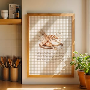 Op de afbeelding: Een ingelijste print met een aquarel illustratie van verschillende broden op een houten plank, met tarwe- en groenaccenten. De achtergrond is een beige en wit geruit patroon. De tekst luidt: "De mens zal niet van brood alleen leven, maar van elk woord dat uit de mond van God komt."