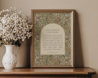 May include: A framed print with the text "LOVE IS PATIENT LOVE IS KIND" in a gold frame. The print has a floral design in green, red, and cream colors. A white vase with white flowers is on the left.