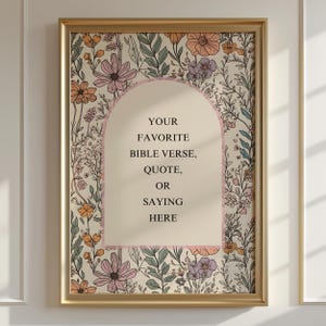May include: A framed print with a gold-coloured frame. The print features a floral design with pink, orange, and purple flowers. The centre has an arch shape with the text: "YOUR FAVORITE BIBLE VERSE, QUOTE, OR SAYING HERE."