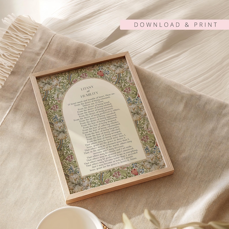 May include: A rectangular wooden frame containing a print of the Litany of Humility. The text is centred within an arched cream-coloured panel, surrounded by a detailed botanical border featuring green leaves and multi-coloured floral patterns.