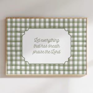 May include: A framed wall art piece with a green and white gingham pattern background. The artwork features a white, ornate-edged center with the text "Let everything that has breath praise the Lord" in a script font. The frame is a light brown color.