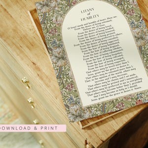 May include: A rectangular print featuring the Litany of Humility prayer in black text centred within an arched cream-coloured frame. The border displays a dense botanical pattern of green leaves, blue flowers, and small red berries on a light background.