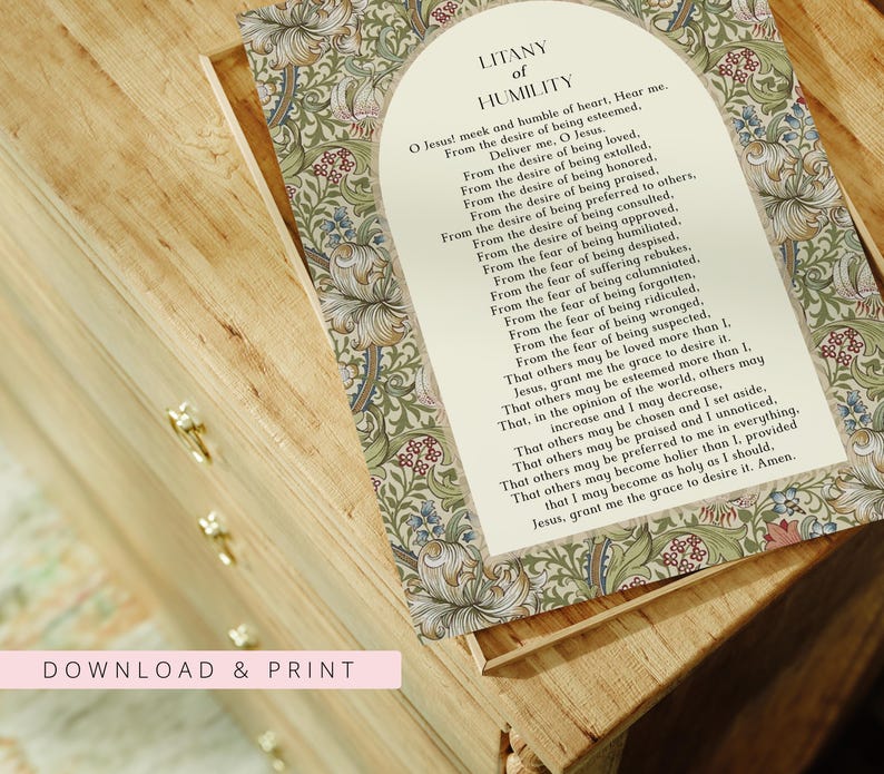 May include: A rectangular print featuring the Litany of Humility prayer in black text centred within an arched cream-coloured frame. The border displays a dense botanical pattern of green leaves, blue flowers, and small red berries on a light background.