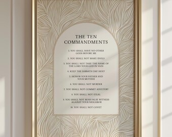 May include: A framed wall art print featuring The Ten Commandments in black text centered within an arched cream-colored panel. The background is decorated with a beige and white abstract leaf pattern. The entire piece is encased in a gold frame.