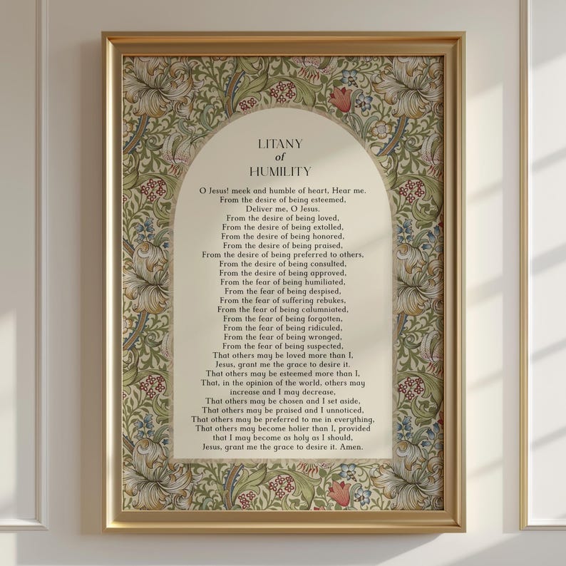 May include: A framed print featuring the Litany of Humility text centred within an arched cream-coloured panel. The border displays a dense botanical pattern of green leaves, scrolling vines, and stylised flowers in shades of tan, red, and blue.