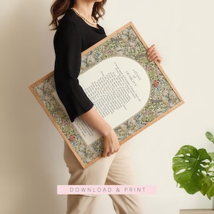 May include: A rectangular framed print featuring the Litany of Humility in black text centred on a white background. The border displays a detailed floral and botanical pattern in shades of green, red, and blue. The frame is a light-toned wood.